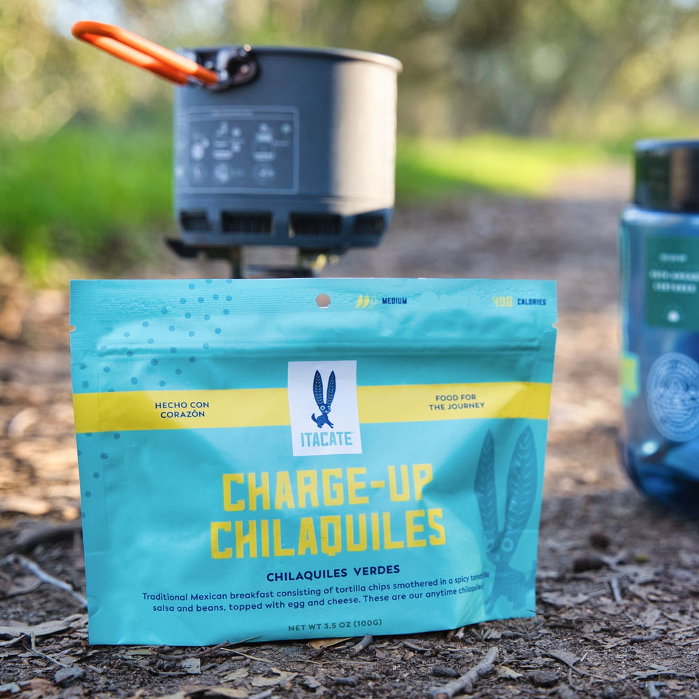 Packaged food items on a natural outdoor setting with a canister stove and bear canister in the background