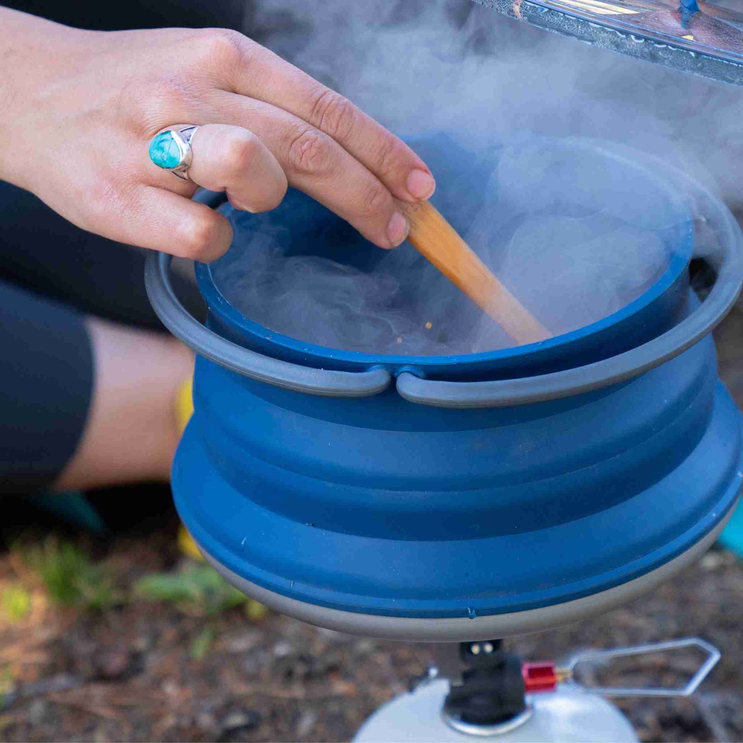 a hand stirring arroz con leche in a pot using a canister camp stove